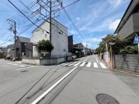 広々とした道路が印象的な街並みです。電線や歩道道路標識なども整備されており周囲の住宅も落ち着いた雰囲気です。天気の良い青空が広がり開放感を感じられます。