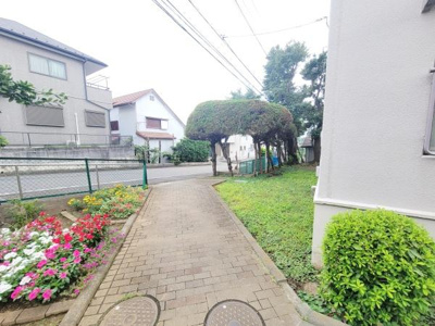敷地内に手入れされた植栽が並び道沿いの花壇が彩りを加えています。緑豊かな雰囲気が感じられる空間です。歩道は広めで歩きやすく周囲も落ち着いた住宅街となっています。