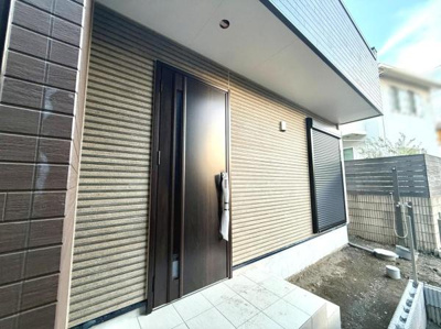 玄関は落ち着いた色合いの外壁と調和したデザインです。広めのアプローチが使いやすい空間を演出しています。ドア横の縦長窓が採光をサポートしています。玄関まわりは開放的でお手入れもしやすい印象です。
