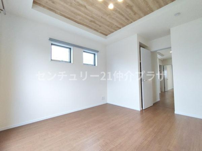 白を基調とした明るい洋室です。温かみのあるフローリングが空間に調和しています。天井のデザインがアクセントになっています。2つの横長の窓が採光を確保しています。開放感のあるレイアウトです。