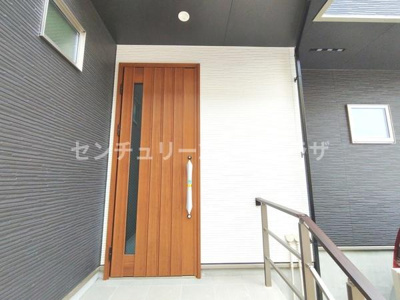 玄関ドアは木目調デザインでモダンな外観にマッチしています。手すり付きのアプローチで昇降しやすい点がポイントです。玄関周囲は清潔感がありシンプルな雰囲気を演出しています。