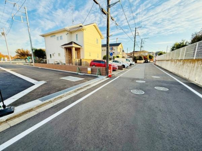 現地の前面道路は舗装されており車の通行もスムーズです。周囲には住宅が並び開放感があります。道路幅も確保されていてすっきりとした印象です。電柱やインフラ設備も整備されています。