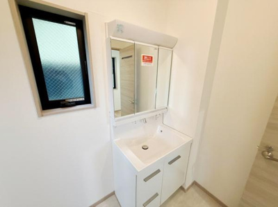 明るい空間に設置された洗面台が日々の身支度を快適にサポートします。三面鏡タイプで収納力も優れています。シンプルで清潔感のあるデザインが特徴です。窓が配置されており換気にも配慮されています。