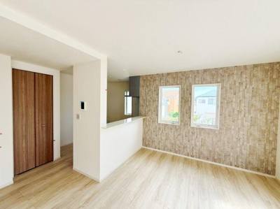 明るい陽射しが差し込むリビングです。木目調のフローリングが空間に温かみをもたらしています。対面キッチン仕様で使い勝手に配慮されたレイアウトです。アクセントクロスが特徴的な内装です。