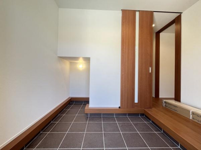 玄関は広々としたタイル仕上げで清潔感があります。木目調の扉とステップが空間に温かみをプラスしています。スタイリッシュな照明がアクセントとなり落ち着いた雰囲気を演出しています。