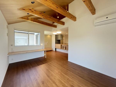木目調の天井梁がアクセントになったリビングです。開放感のある空間が広がります。大型窓から明るい光が差し込みます。キッチンと繋がる間取りが特徴的です。シンプルな内装でインテリアも楽しめます。