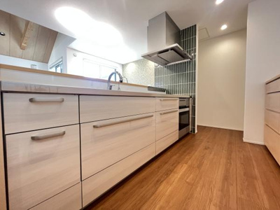 明るい木目調とホワイトがバランス良く調和したキッチンです。広々とした通路幅で作業がしやすい設計となっています。収納スペースも多くすっきりした印象です。床の色合いが全体をやさしくまとめています。