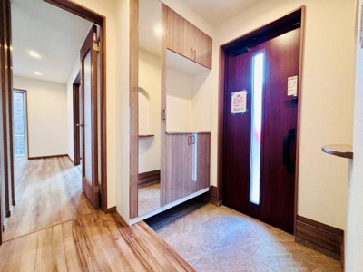 すっきりとした玄関スペースが印象的です。木目調の床と収納が統一感を生み出しています。大型のシューズボックスが備えられており収納力に優れています。玄関ドアの縦型ガラススリットから自然光が差し込みます。