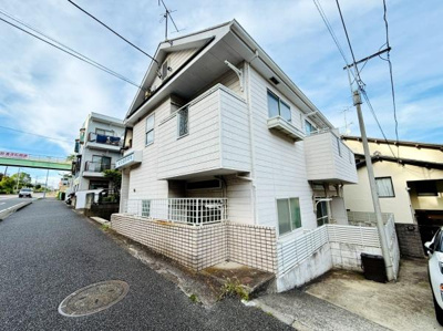 道沿いに建つ白を基調とした外観が印象的です。複数のバルコニーがあり各部屋に採光が期待できます。角地に位置しているため外観の開放感が感じられます。敷地のフェンスや塀がしっかりと設けられています。