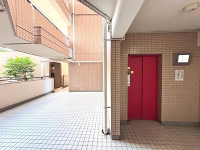 明るい共用部が印象的な空間です。赤いエレベーターがアクセントになり移動も便利に感じられます。タイル張りの床で清潔感があります。敷地内には緑も配置されています。余裕のある動線設計です。