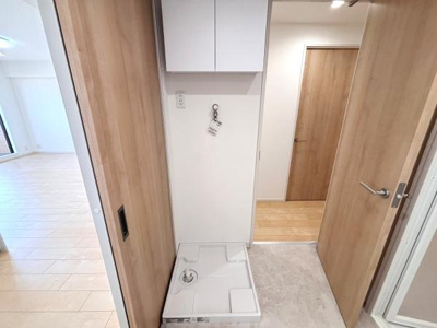 洗濯機置き場がすっきりと設けられており収納スペースも備わっています。木目調のドアがナチュラルな雰囲気を演出しています。隣接するフローリングの空間も明るく広々としています。動線が確保された間取りです。