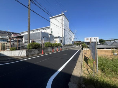 前面道路は幅員がしっかり確保されており車の出入りも安心です。電線や設備も整備されており周辺環境も整っています。現地は日当たりも感じられる開放的な雰囲気です。道路沿いの緑もアクセントになっています。