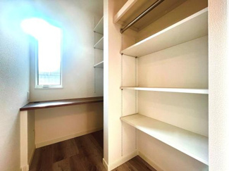 明るい窓から光が差し込む収納スペースです。可動式の棚とハンガーパイプが備わり衣類や小物類も整理しやすい設計です。作業台スペースもあり使い勝手の幅が広がります。開放感のある空間が特徴です。