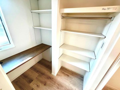 棚とハンガーパイプが備わった収納スペースです。採光を取り入れた窓があり明るい空間になっています。床材との調和も感じられる仕様です。カウンターも設けられており整理整頓に役立ちます。
