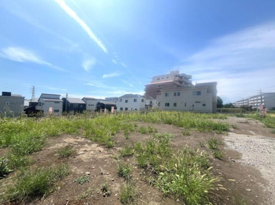 開放感のある現地土地写真です。青空が広がり周辺には住宅や建物が並んでいます。土地の形状が分かりやすく現地の様子をしっかりと確認いただけます。前面道路にもアクセスしやすい環境となっています。