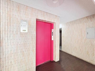 明るい色合いのエレベーターがアクセントになっています。エントランスや共用部の壁はタイル仕上げで清潔感があります。床はダークカラーで落ち着いた雰囲気です。エレベーターホールが広めに確保されています。