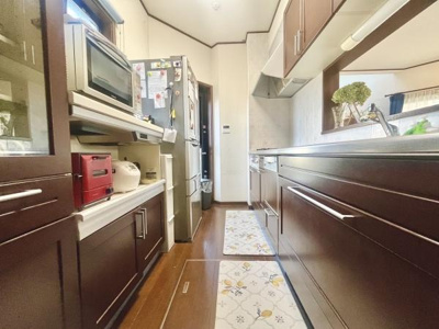 落ち着いた色合いの収納が空間を引き締めます。窓からの自然光が入り明るい印象です。収納スペースが豊富で整理整頓しやすいキッチンです。調理台も広めに確保されています。