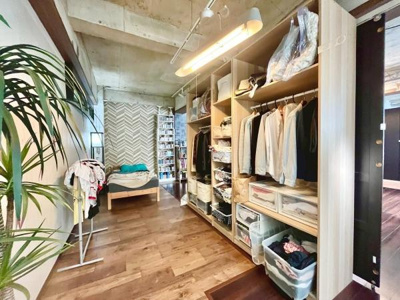 開放的な収納スペースがベッドルームの使い勝手を高めています。天井のコンクリートと木目の床がスタイリッシュな雰囲気を演出します。奥行きのある空間で整理整頓がしやすそうです。インテリアの自由度も魅力です。