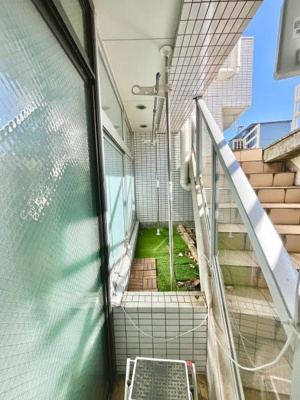 明るい日差しが差し込むバルコニーです。ガラスパネルの柵が開放感を演出しています。床のタイルと人工芝がアクセントとなり清潔感があります。物干し用ポールが設置されているので便利です。