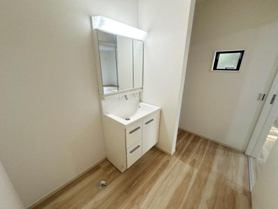 明るい照明の付いた洗面台が設置されています。収納スペースも豊富ですっきりとした空間です。木目調の床が全体に温かみをプラスしています。窓もあり通気性にも配慮されています。