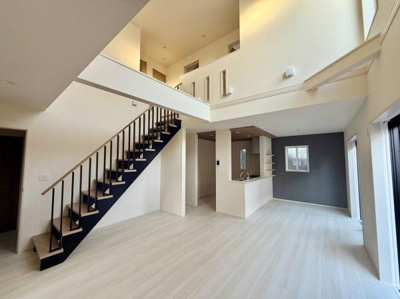 吹き抜けの天井が開放感を演出しているリビングです。大きな窓から光が差し込み室内を明るくします。シンプルな色合いが洗練された印象を与えます。階段や壁のデザインもポイントです。