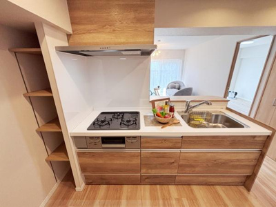 木目調のキャビネットが落ち着いた雰囲気を演出しています。使い勝手の良いワークトップが特徴です。ガスコンロとシンクが横並びで効率的なレイアウトです。横には便利な可動棚が設置されています。