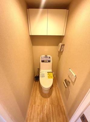 清潔感のあるトイレ空間です。収納棚が設置されており物の整理整頓がしやすい仕様です。木目調の床が温かみを感じさせる雰囲気です。壁に備え付けのペーパーホルダーも使いやすい配置です。