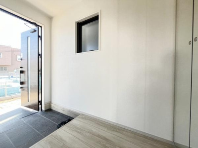 玄関には窓が設置されているため採光がしっかり確保されています。広々としたスペースが特徴的です。モダンな印象の玄関ドアが採用されています。ホワイトを基調とした内装が明るい雰囲気を演出しています。