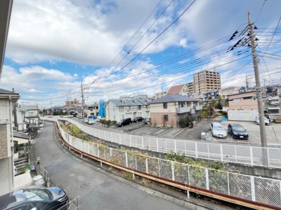 現地からの眺望が広がる開放感のある景色です。周辺には住宅や駐車場があり落ち着いた環境が広がっています。青空が広がる空間で遠くまで見渡せます。電線や道路もしっかり整備されている様子が見える眺めです。