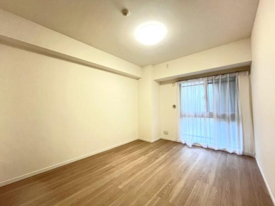 ナチュラルな色合いの床が洋室全体に落ち着いた印象を与えています。大きな窓から自然光が入りやすい設計です。壁や天井がホワイトで統一されており空間が広く感じられます。