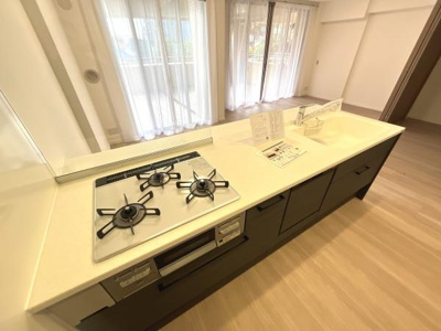 開放感のあるキッチンが特徴です。ガスコンロが3口あり調理が快適に行えます。収納スペースも豊富で整理しやすいです。明るい室内が印象的な空間です。使いやすさを感じられるレイアウトです。