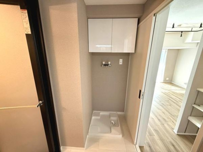 洗濯機置き場がしっかり確保されており上部には収納できるキャビネットが設置されています。床は清潔感のあるタイル仕様で移動もスムーズです。隣接したリビングとの行き来もしやすい空間です。