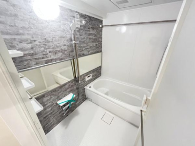 スタイリッシュなデザインのバスルームです。壁面のタイル調パネルがアクセントとなり洗練された印象です。大きな鏡が空間を広く見せます。収納棚もしっかり備わっています。清潔感のある白を基調とした内装です。