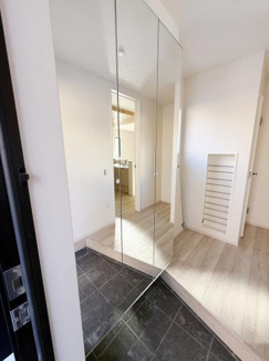 玄関は明るく開放的な印象です。大きなミラーが空間に奥行きを与えすっきりとしたデザインになっています。白を基調とした壁と床が清潔感を感じさせます。収納スペースも設けられており機能面にも配慮されています。