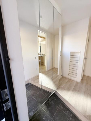 玄関は明るく開放的な印象です。大きなミラーが空間に奥行きを与えすっきりとしたデザインになっています。白を基調とした壁と床が清潔感を感じさせます。収納スペースも設けられており機能面にも配慮されています。