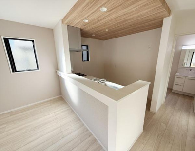 木目調の天井が印象的なキッチンです。窓から自然光が入り明るい雰囲気になっています。対面式のカウンターで開放感があります。白を基調とした空間がすっきりとしています。隣室との動線もスムーズです。